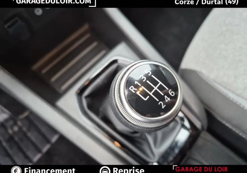 Gros plan sur le levier de vitesse manuel noir de la Renault Clio gris clair, avec marquages blancs visibles.