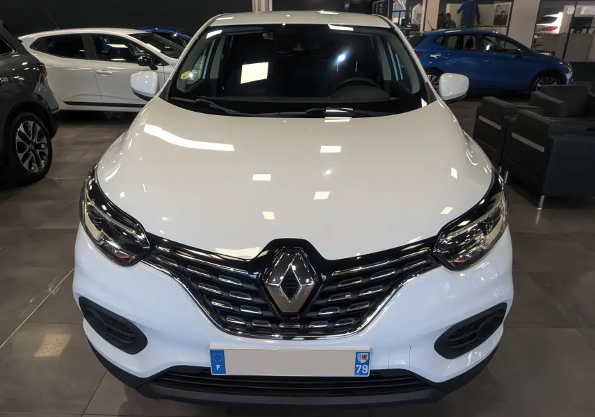 Vue avant d'un Renault Kadjar blanc Glacier 2021 en showroom, mettant en valeur sa calandre chromée et ses phares LED.