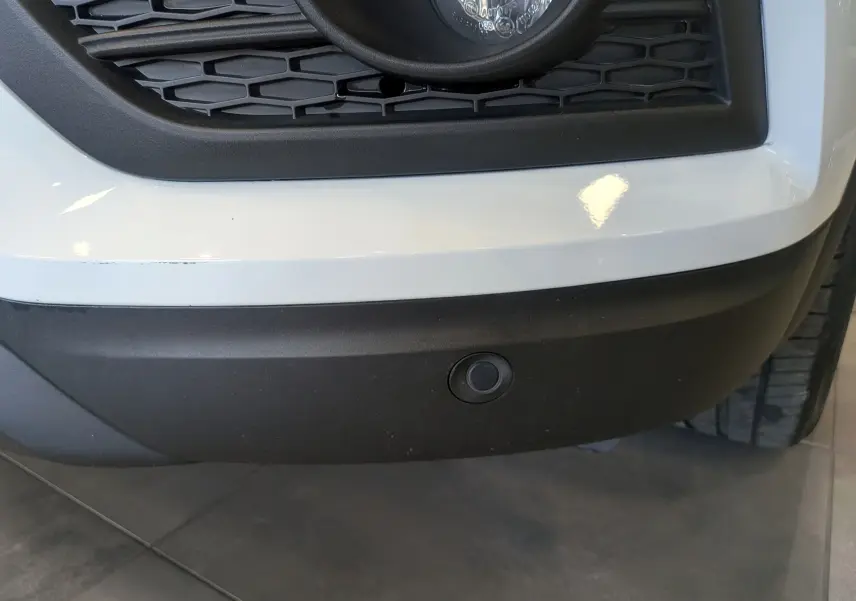 Gros plan sur le pare-chocs avant blanc glacier du Renault Kadjar avec capteur de stationnement noir intégré.
