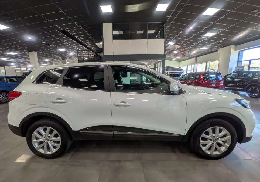 Vue de profil côté gauche d'un Renault Kadjar blanc Glacier 2021 en showroom, avec jantes alliage et vitres teintées.