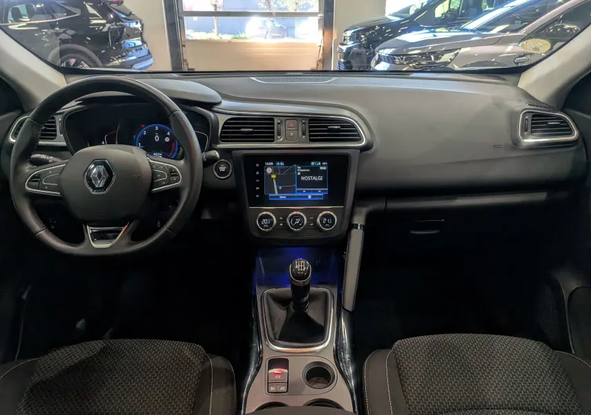 Vue intérieure frontale du tableau de bord du Renault Kadjar 2021 avec volant, écran tactile et levier de vitesses manuel.