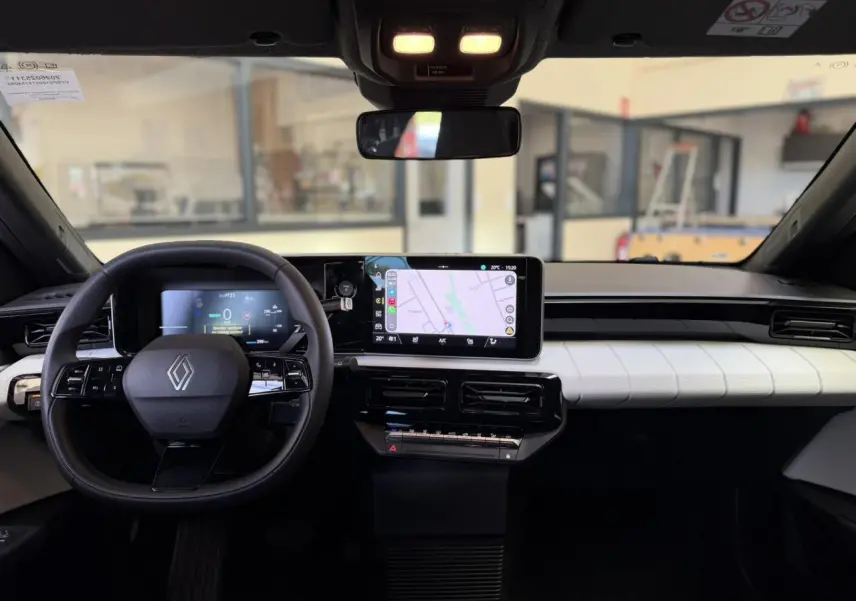 Vue intérieure frontale du tableau de bord noir et blanc de la Renault R5 E-Tech avec écran tactile et volant multifonction.
