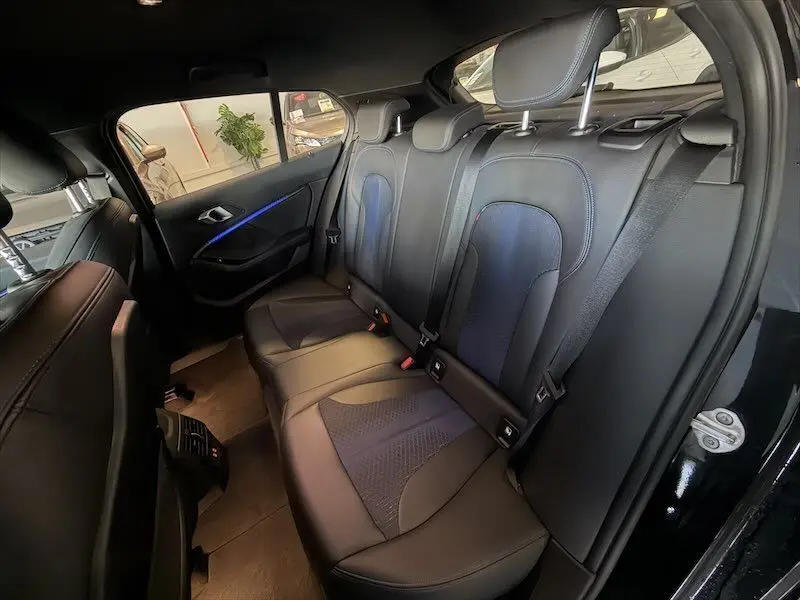 Vue intérieure arrière droite de la BMW Série 1 noire métal, sièges en cuir noir avec inserts tissu bleu et éclairage d'ambiance bleu.
