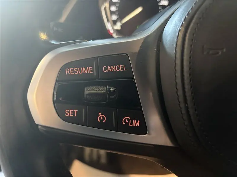 Gros plan sur les commandes de régulateur de vitesse au volant d'une BMW Série 1 noire, boutons rétroéclairés rouges.