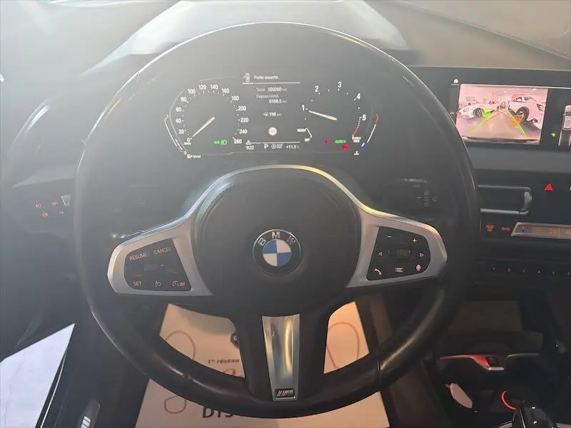 Vue rapprochée du volant cuir noir M Sport d’une BMW Série 1 118d avec tableau de bord digital et écran de caméra de recul.