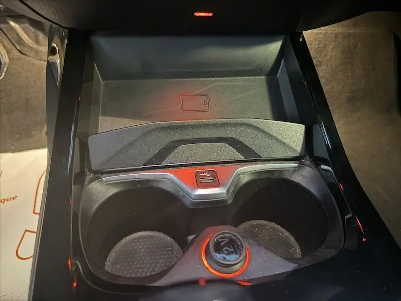 Gros plan intérieur sur la console centrale noire avec porte-gobelets et prise USB éclairée en rouge dans une BMW Série 1.