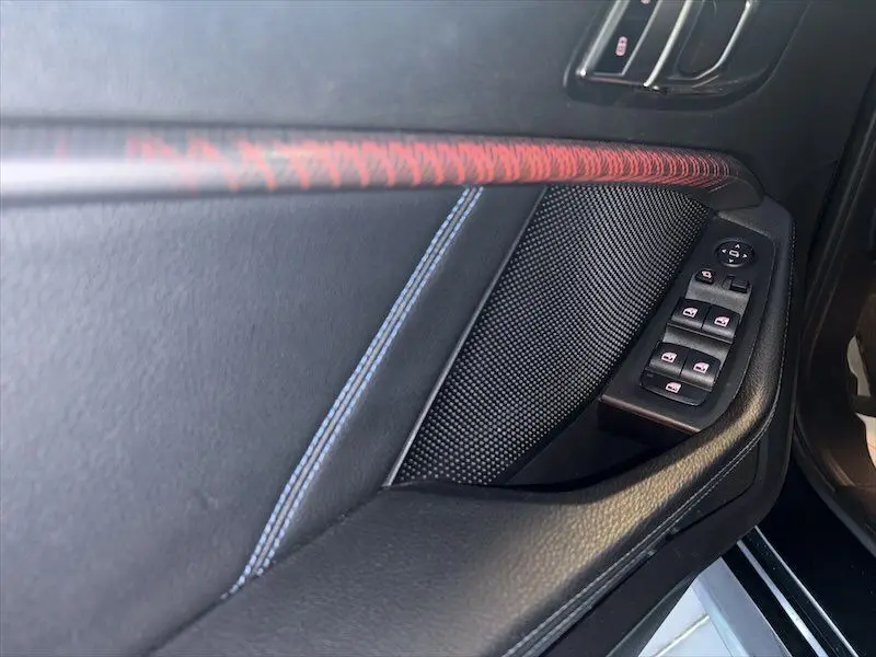 Détail de la porte côté conducteur de la BMW Série 1 noire, avec commandes de vitres et surpiqûres bleues et rouges.