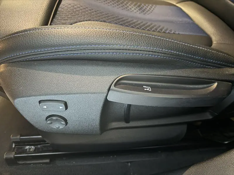 Détail côté gauche du siège avant noir avec commandes de réglage manuel et électrique sur BMW Série 1 noire.