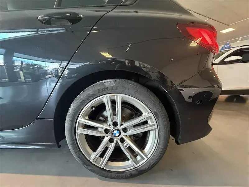 Gros plan sur la roue arrière droite d'une BMW Série 1 noire métal, avec jante alliage M Sport visible en intérieur showroom.