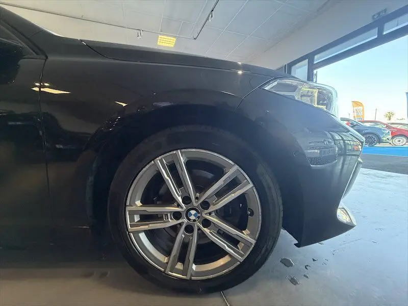 Gros plan sur la roue avant gauche et l’aile d’une BMW Série 1 noire métal, avec jante alliage et phare avant visible.