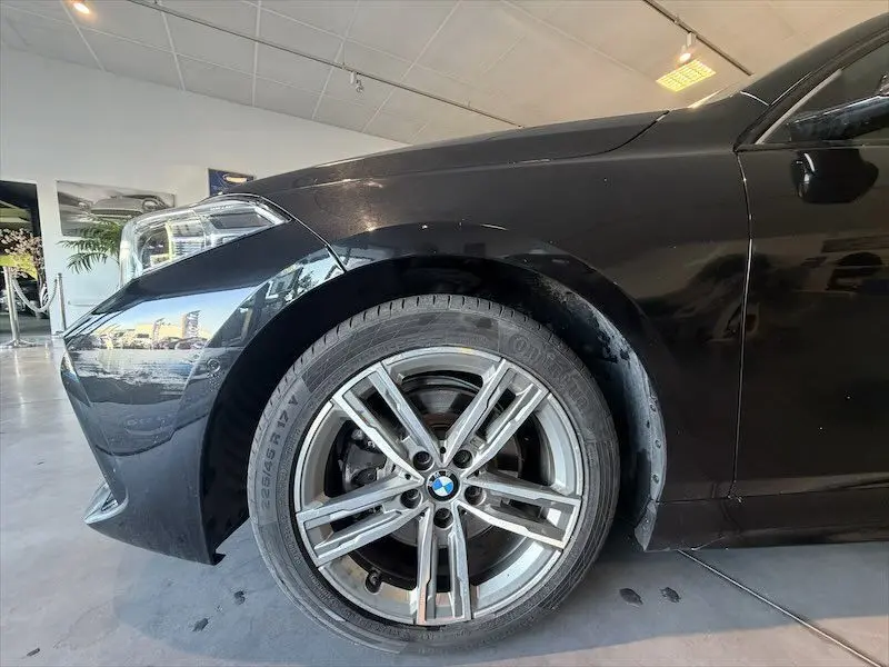 Gros plan sur la roue avant gauche d'une BMW Série 1 noire métal, avec jante alliage M Sport visible en intérieur showroom.