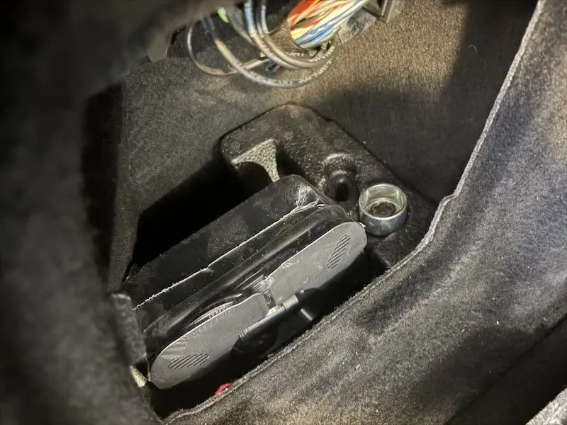 Gros plan sur un boîtier électronique et câblage dans l’espace moteur d’une BMW Série 1 noire métal.