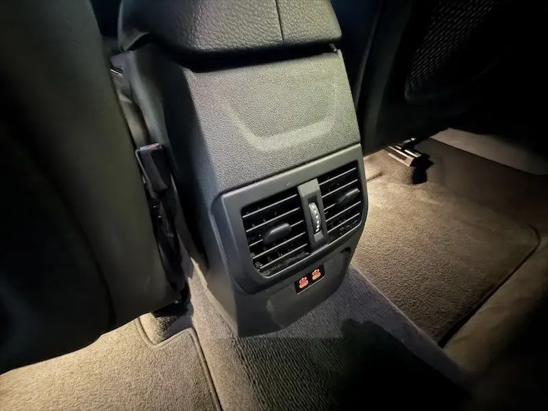 Détail des aérateurs et commandes de sièges chauffants à l'arrière d'une BMW Série 1 noire, vue depuis le sol côté arrière.