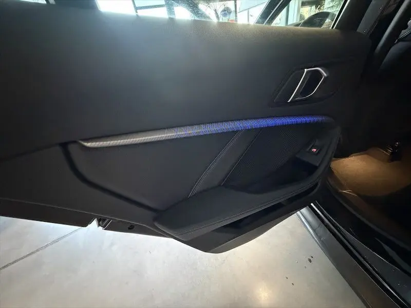 Vue intérieure côté gauche de la porte noire métal de la BMW Série 1 avec éclairage d'ambiance bleu et poignée argentée.