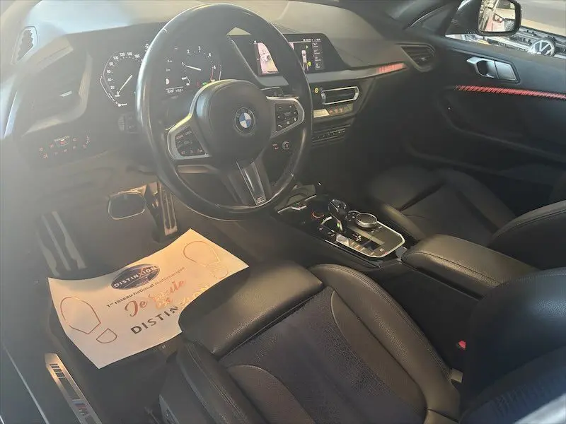 Vue intérieure côté conducteur de la BMW Série 1 noire, mettant en valeur le volant M Sport et la console centrale moderne.