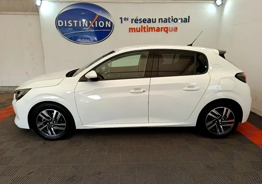 Profil droit d'une Peugeot 208 blanche 2021 PureTech 100 S&S Allure Business en intérieur avec jantes alliage noires et grises.