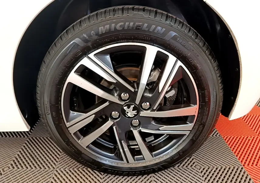 Gros plan sur la roue avant droite blanche d'une Peugeot 208 avec jante alliage bicolore et pneu Michelin.