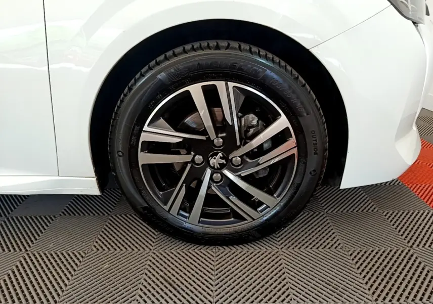 Gros plan sur la roue avant droite d’une Peugeot 208 blanche, mettant en valeur la jante alliage noire et argent.
