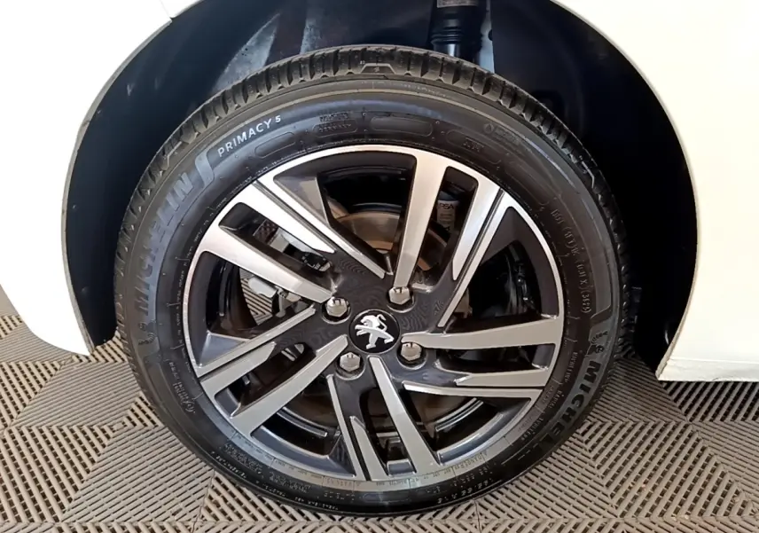 Gros plan sur la roue avant droite d'une Peugeot 208 blanche, mettant en valeur la jante alliage bicolore et le pneu Michelin.