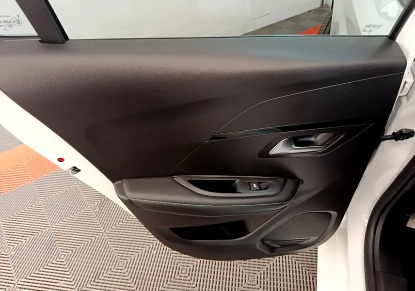 Vue rapprochée de la porte arrière droite noire avec poignée et bouton de lève-vitre d’une Peugeot 208 blanche.