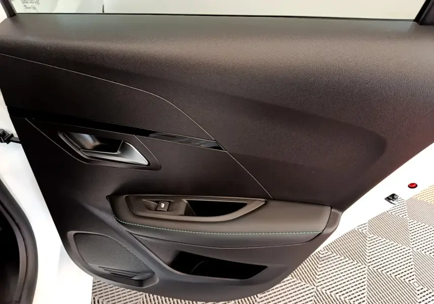 Détail de la porte intérieure côté gauche d’une Peugeot 208 blanche, avec poignée argentée et commande de vitre.