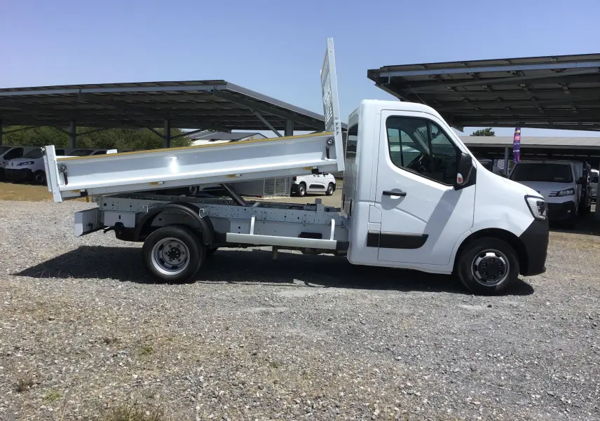 Renault Master benne blanche vue de profil côté gauche, benne relevée et roues jumelées arrière visibles.