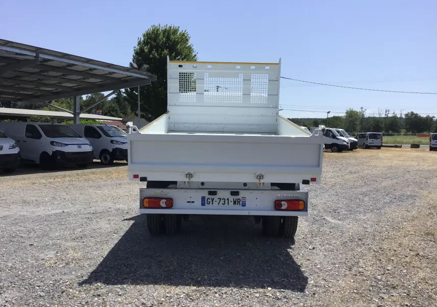 Vue arrière d’un Renault Master blanc avec benne basculante et roues jumelées sur un terrain extérieur.