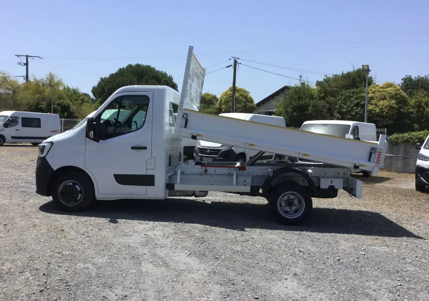 Vue de profil côté gauche d’un Renault Master blanc avec benne basculante relevée sur un terrain extérieur.
