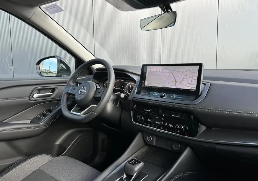 Vue intérieure côté conducteur du Nissan Qashqai 2025, tableau de bord noir avec écran tactile et volant cuir multifonction.