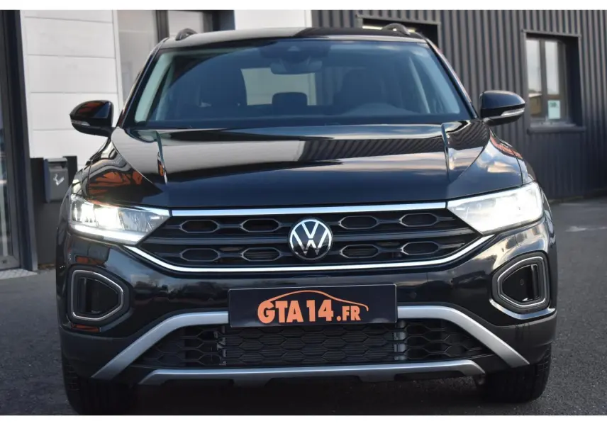 Vue frontale du Volkswagen T-Roc 2025 noir grenadilla avec phares LED allumés et calandre hexagonale distinctive.