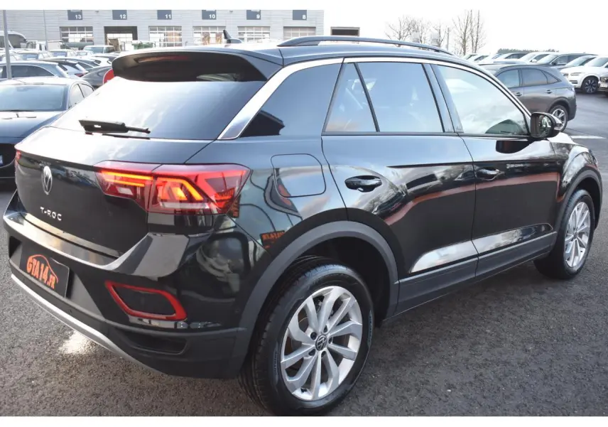 Vue 3/4 arrière droite du Volkswagen T-Roc noir métallisé avec jantes alliage 17 pouces et feux arrière LED allumés.