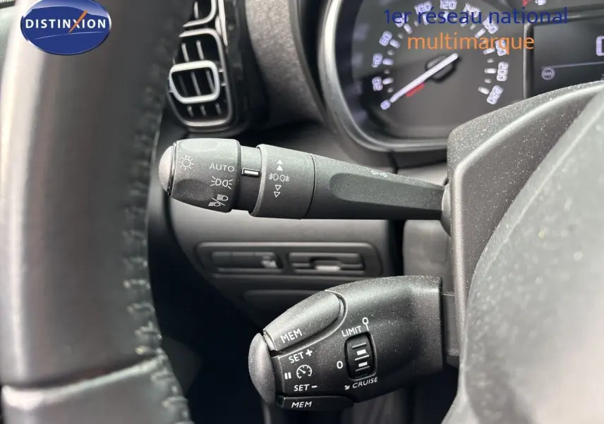 Gros plan sur les commandes au volant d'une Citroën C3 Aircross gris platinium, mettant en valeur les fonctions de régulateur et éclairage.