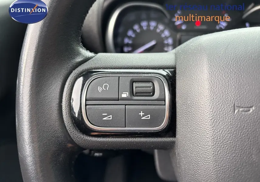 Gros plan sur les commandes gauche du volant en cuir noir du Citroën C3 Aircross 2021, avec tableau de bord flou en arrière-plan.