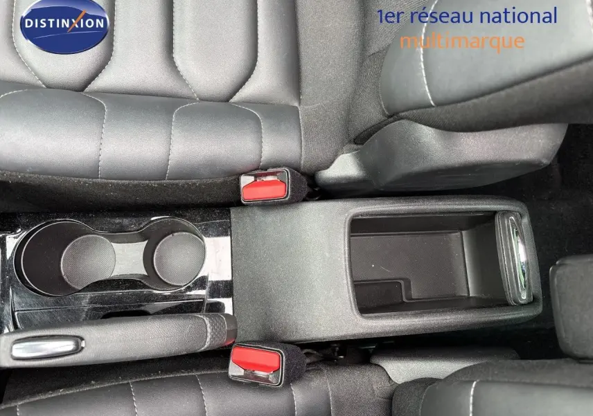 Vue plongeante sur la console centrale noire avec porte-gobelets et accoudoir entre les sièges avant en cuir noir.