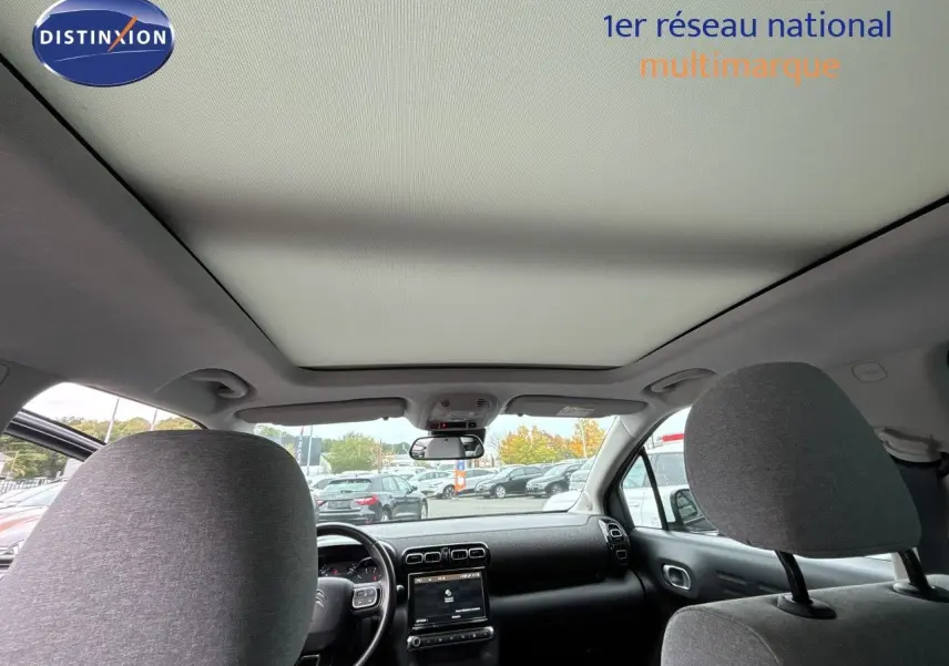 Vue intérieure avant du Citroën C3 Aircross gris, montrant le tableau de bord et le grand toit panoramique.