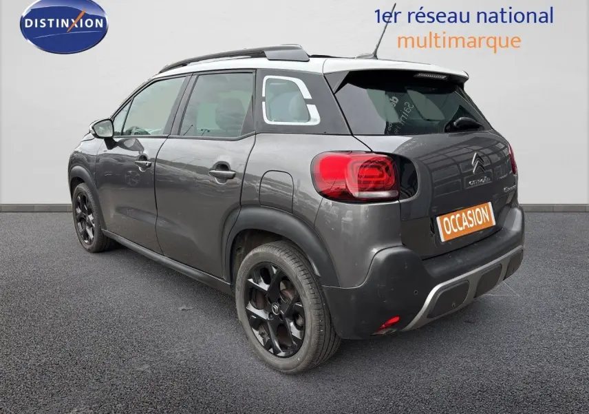 Vue 3/4 arrière droite d'un Citroën C3 Aircross gris platinium avec toit blanc et jantes noires distinctives.