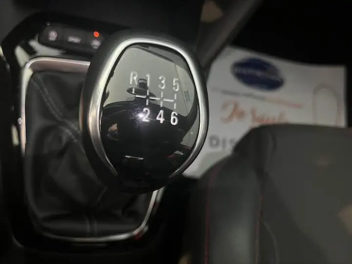 Le levier de vitesse manuel noir de l'Opel Corsa rouge Kardio, avec marquages blancs visibles en gros plan.