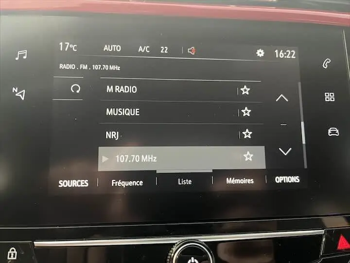 Écran tactile central de la console d'une Opel Corsa rouge Kardio, affichant la radio FM sur 107.70 MHz.