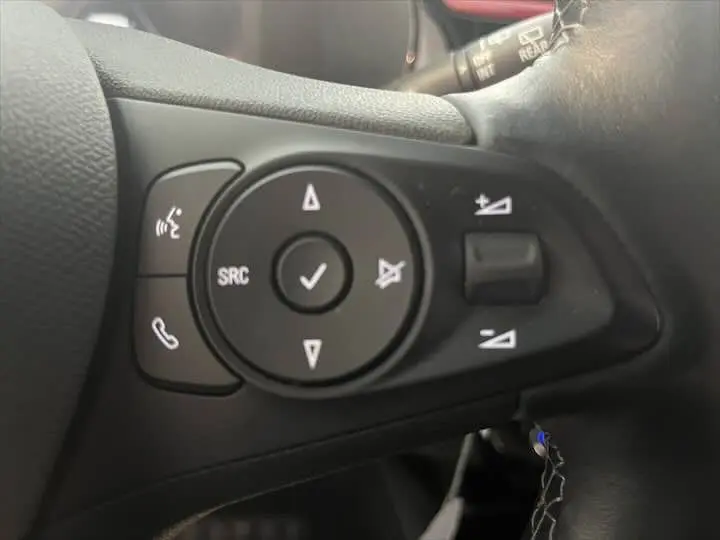 Gros plan sur les commandes au volant noir de l'Opel Corsa 1.2T 100 CH S&S GS-LINE, intérieur rouge et noir visible en arrière-plan