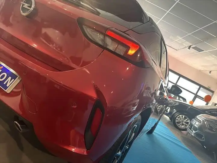 Vue 3/4 arrière gauche d'une Opel Corsa rouge Kardio 2021 en showroom, avec feux arrière allumés et jantes noires.
