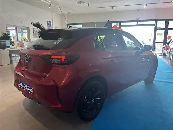 Vue 3/4 arrière droite d'une Opel Corsa rouge Kardio en showroom, avec jantes noires et toit noir contrastant.