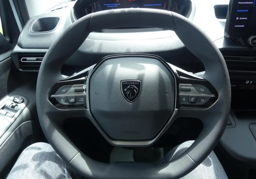 Volant multifonctions noir de Peugeot Partner 2025 vu de face avec tableau de bord numérique en arrière-plan.