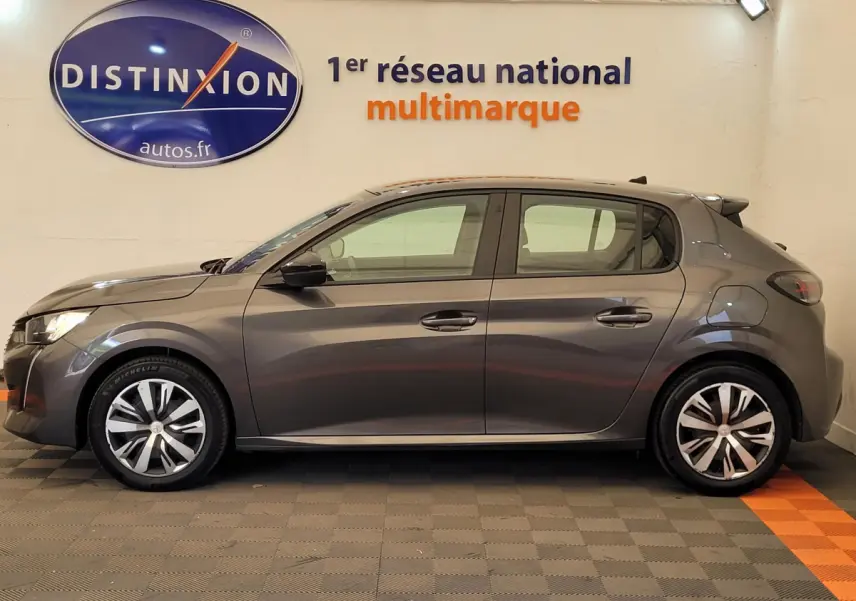 Profil côté gauche d'une Peugeot 208 BlueHDi 100 S&S Active Pack gris foncé, en intérieur sur sol carrelé.