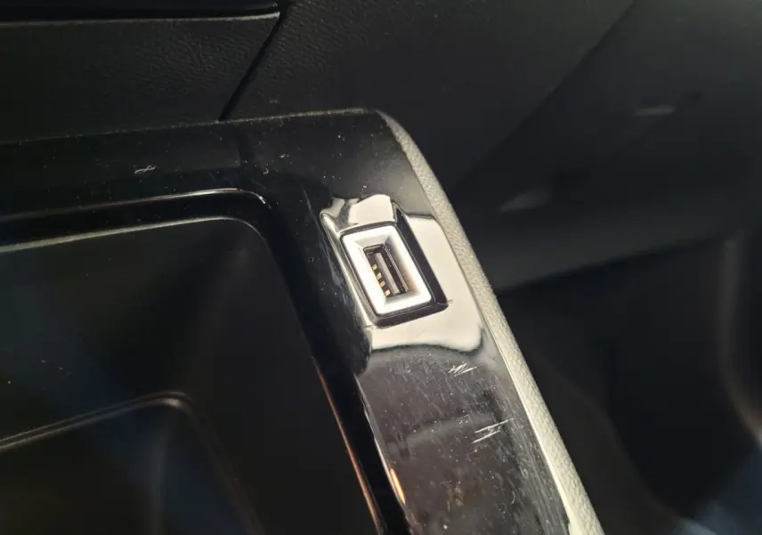 Gros plan sur un port USB intégré dans la console centrale noire d'une Peugeot 208 gris foncé 2023.