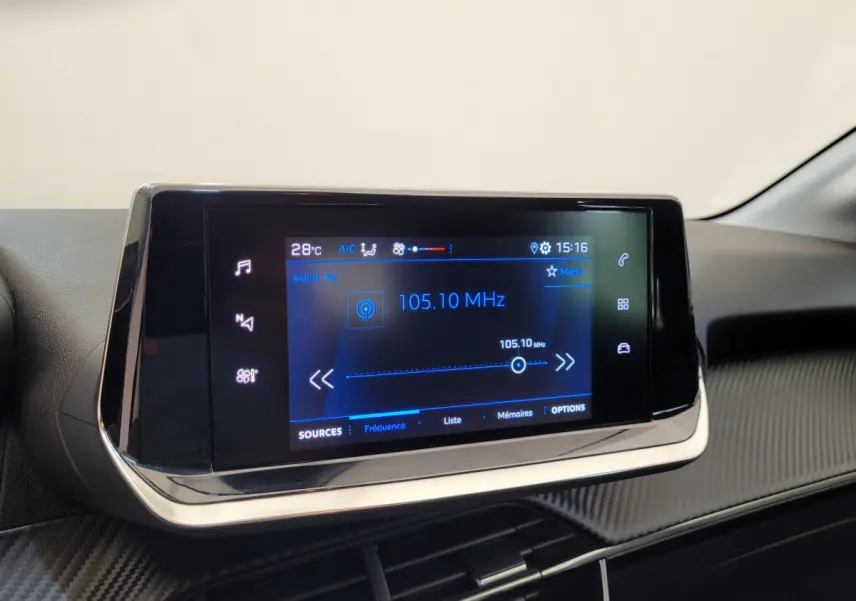 Écran tactile central de la Peugeot 208 gris foncé, affichant la radio FM à 105.10 MHz en intérieur.