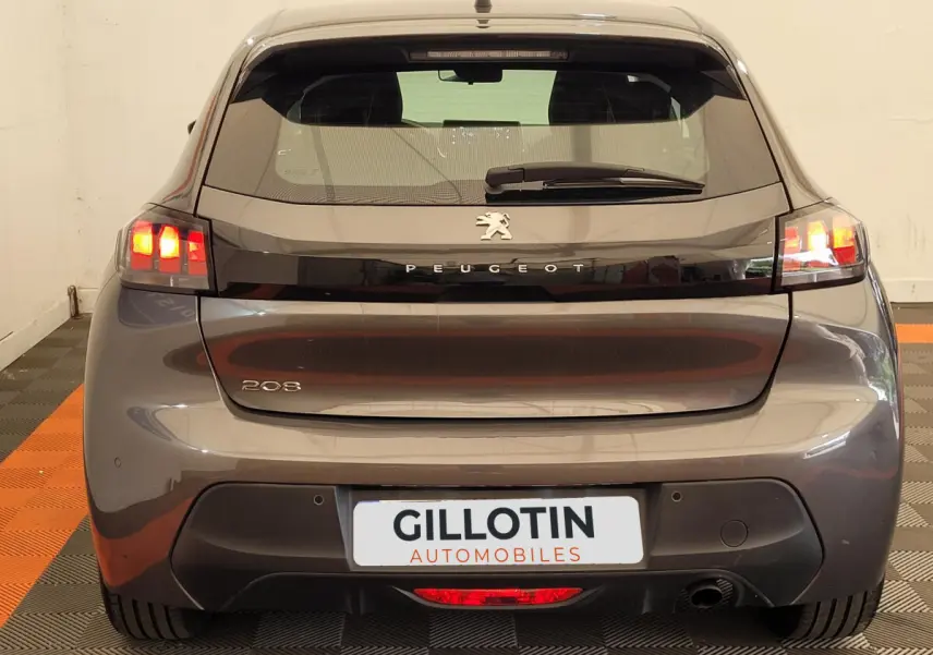 Vue arrière d'une Peugeot 208 gris foncé 2023 avec feux allumés et plaque d'immatriculation GILLOTIN AUTOMOBILES.