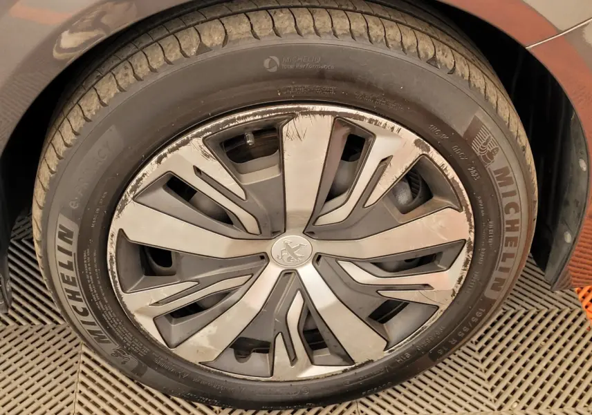 Gros plan sur la roue avant gauche d'une Peugeot 208 gris foncé avec jante alliage au design moderne et pneus Michelin.