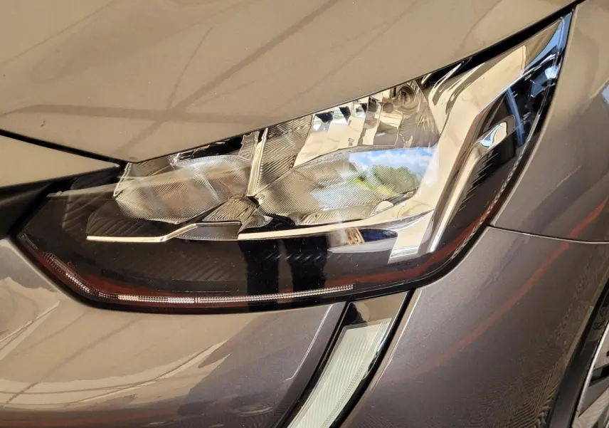 Gros plan sur le phare avant droit d'une Peugeot 208 gris foncé 2023 avec détails LED et carrosserie brillante