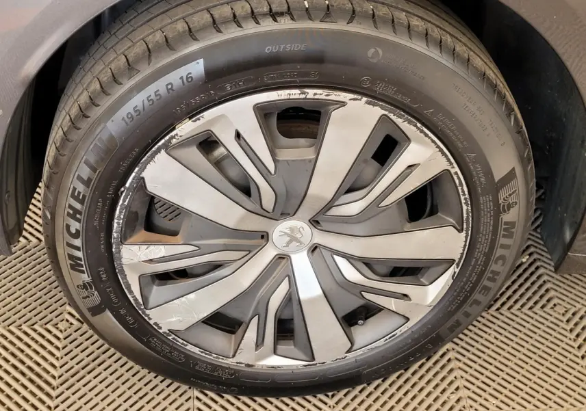 Gros plan sur la jante avant droite gris argenté d'une Peugeot 208 gris foncé avec logo lion central.