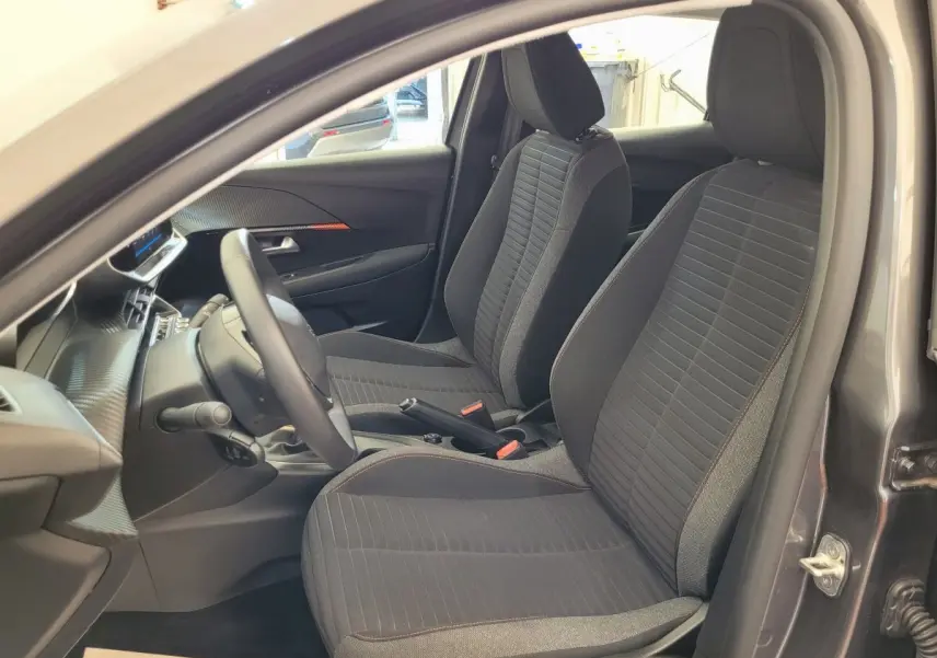 Intérieur vue côté conducteur de la Peugeot 208 gris foncé 2023, sièges tissu noir avec surpiqûres rouges.